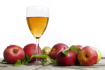 apple juice in a glass and red apples with leaves on old wood, w