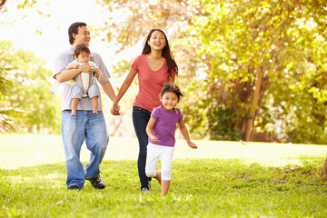 Fototapeta premium Family With Baby In Carrier Walking Through Park