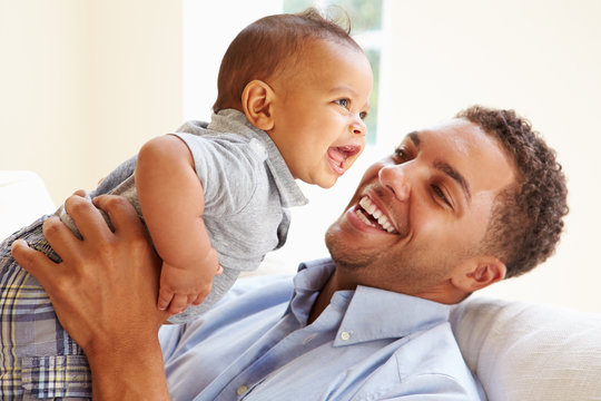 Smiling Father Playing With Baby Son At Home