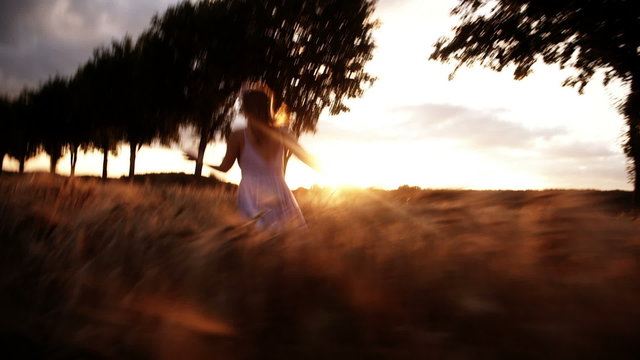 Woman with flower crown running in wheat field during sunset