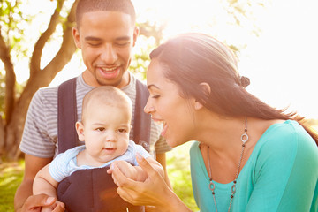 Family With Baby Son In Carrier Walking Through Park
