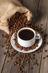 Coffee cup and bag with coffee beans on wooden table.