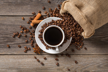 Coffee cup with cinnamon sticks and coffee bag on wooden table.