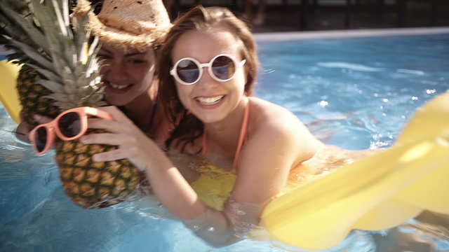 Girls having a silly time with pineapples in swimming pool