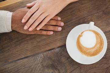 Couple holding hands beside cappuccino