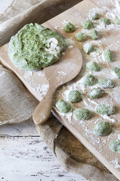 uncooked homemade spinach dumplings on wooden board with dough