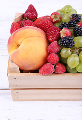 Different berries and fruits in box on wooden table close-up