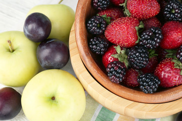 Ripe fruits and berries in bowl on table close up