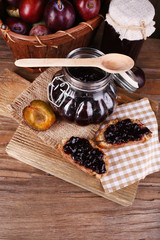 Tasty plum jam in jars and plums on wooden table close-up