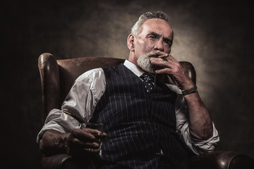 In chair sitting senior business man with cigar and whisky. Gray