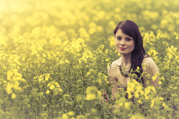 Beautiful woman in meadow of yellow flowers sitting down