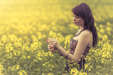 Beautiful woman in meadow of yellow flowers holding flower
