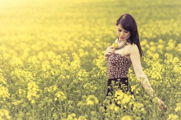 Beautiful woman in meadow of yellow flowers touching flower