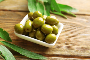 Green olives in bowl with leaves on table close-up