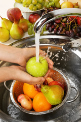 Woman's hands washing apple and other fruits in colander in
