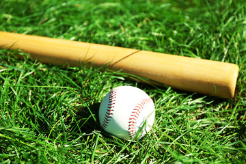 Baseball bat, ball and glove on green grass background
