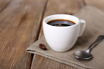 Cup of coffee and coffee beans on napkin on wooden background