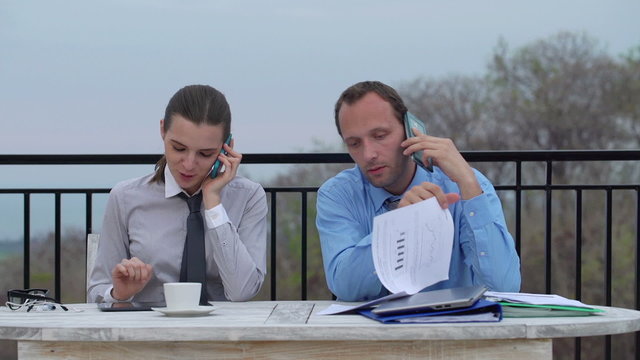 Business couple talking on cellphone, reading documents on terra