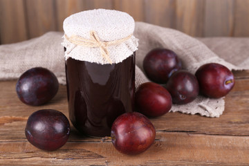Tasty plum jam in jar and plums on wooden table close-up