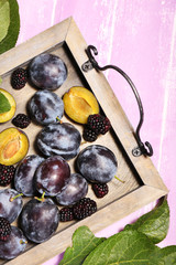 Ripe sweet plums on tray, on pink wooden table