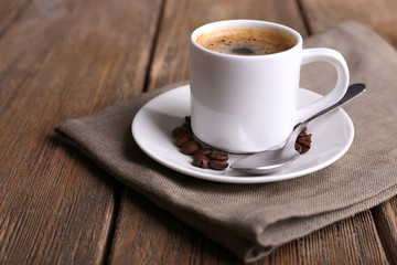 Cup of coffee and coffee beans on napkin on wooden background