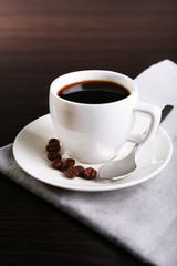 Cup of coffee and coffee beans on napkin on dark background