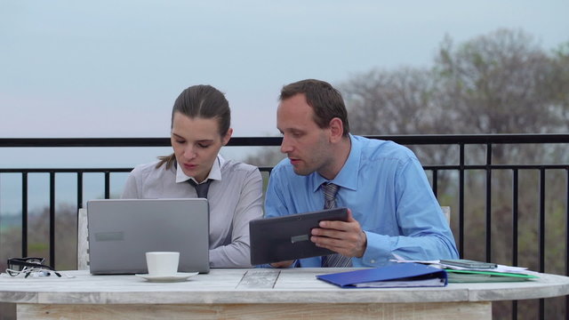 Business couple talking over laptop and tablet computer on terra
