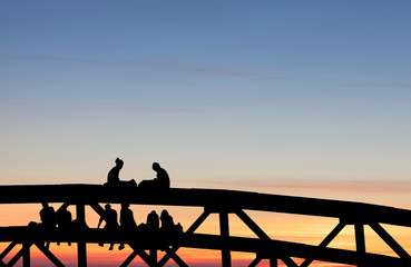 silhouetted teenagers sitting on bridge in sunset