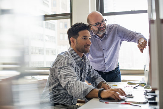 Office life. Two men in an office, using a computer screen. 