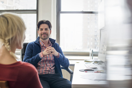 Office life. A man and woman in an office, seated talking to each other. 