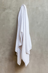 Obraz premium White towel is hanging on the exposed concrete wall in the bathr