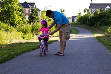 Obraz premium Little girl learning how to ride a bike with her dad