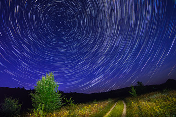 Alone tree on night sky with stars, startrails and country road - 70726135