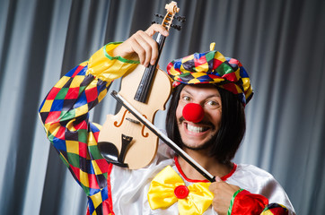 Funny clown plyaing violin against curtain