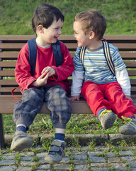 Two children boys, friends or brothers sitting on a bench