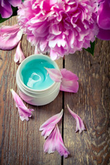 Organic face cream with peonies on an old wooden table, closeup