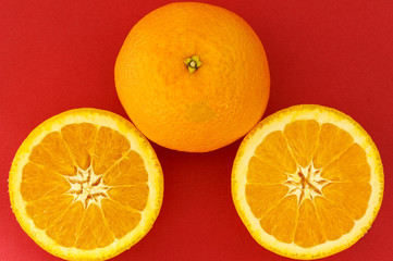 Photo of an orange on a red background, also an orange that is cut in half to show the inside
