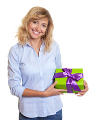 Lachende Frau mit blonden Locken hält ein Geschenk