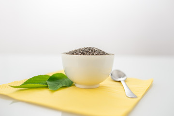 Bowl of dried chia seeds with fresh green leaves