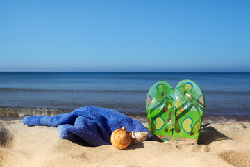 flip flops, towel and seashell on sand beach