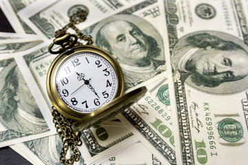 Pocket watch and dollar bills on background.