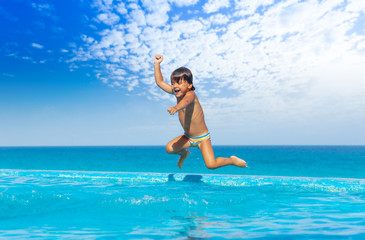 Boy jumps in swimming pool with seaside background