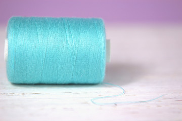 Turquoise, thread on white wooden and lilac background