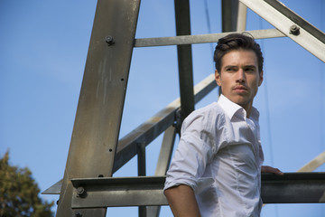 Handsome young man hanging from metal electricity trellis