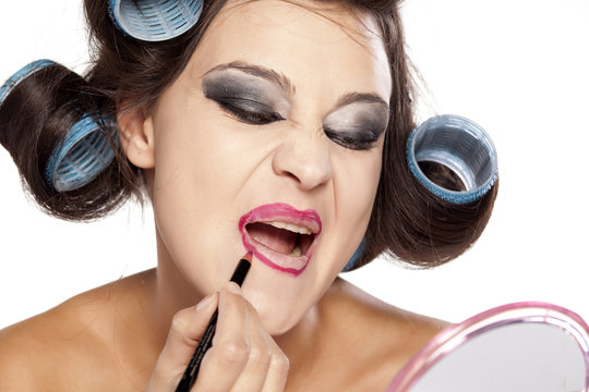 Funny woman with curlers and bad makeup applied lip pencil