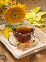 glass cup with tea on a tray with autumn leaves and flowers