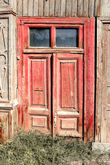 Aged red door with two glass windows on the top in old slum