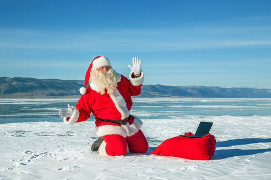 Santa Claus sitting on snow, looking at laptop news