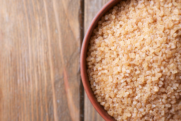Brown crystal sugar in bowl on wooden background