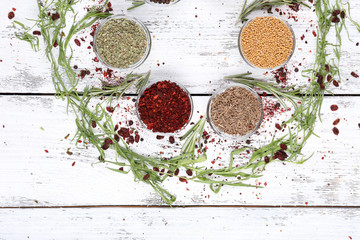 Spices in glass round bowls with herbs on wooden background